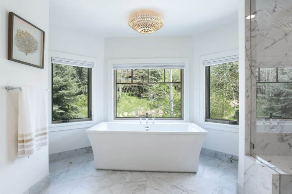 Bathtub in a custom built bathroom with windows leading to a forest